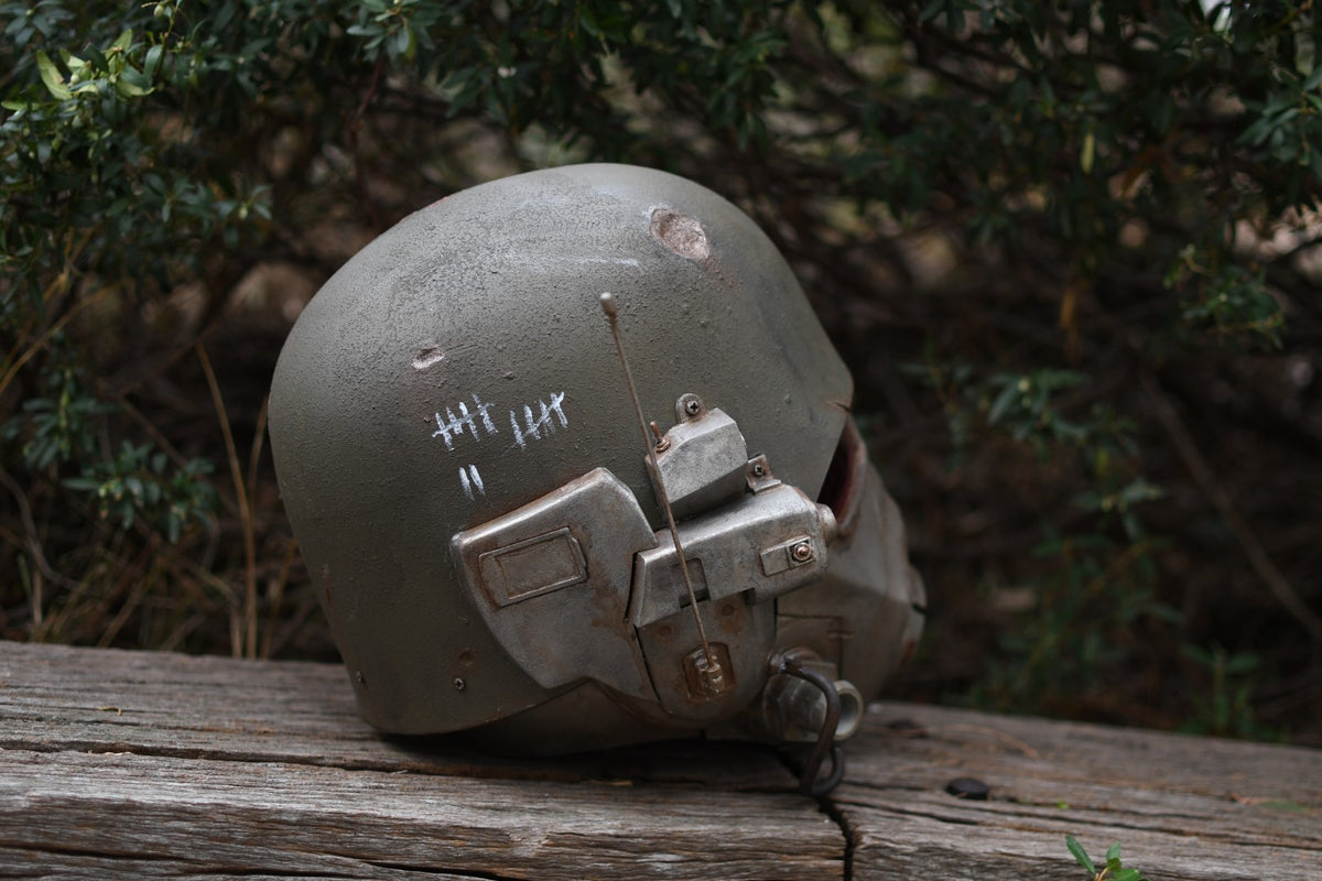 Military helmet with attached communication device on a wooden surface with greenery in the background