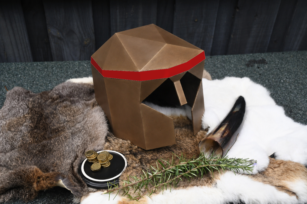 A low-poly style brown helmet with a red band sits on animal fur and a dark textured surface, styled with a horn, coins, rosemary, and a small round dish.